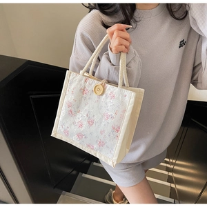 Close-up of cream handbag featuring delicate pink floral lace embroidery and wooden button