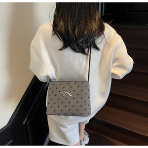 Close-up of small dark gray polka dot crossbody bag with a silver metal bow clasp