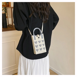 Detail of a cream knit mobile phone bag featuring grey heart patterns and a round handle