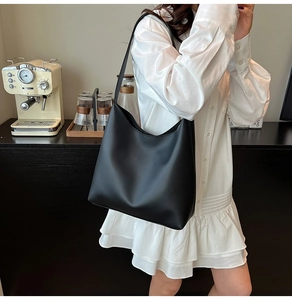 Detail of minimalist black large capacity faux leather tote bag worn as a shoulder bag