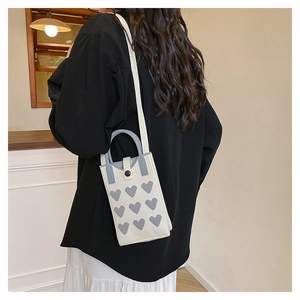 Close-up of knit mini phone bag in cream and grey with heart pattern and shoulder strap