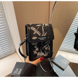 Detailed view of women's black leaf pattern crossbody bag with round metal charm