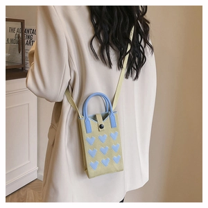 Detail of knitted cream mini bag featuring light blue heart patches and shoulder strap