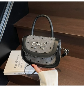 Close-up of gray polka dot handbag with silver bow metal buckle and black leather trim