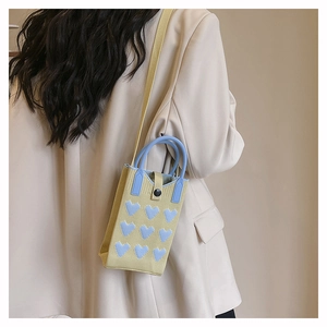 Detailed side view of yellow knitted phone bag with 3D blue hearts and strap on model