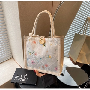 Detail of floral embroidery on lace handbag with wooden button and woven handle