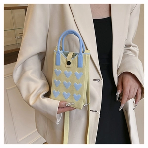 Detail of yellow knitted heart-pattern bag with baby blue handles and crossbody strap