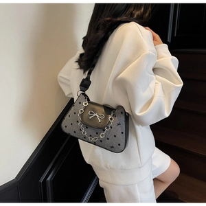 Detail of grey polka dot underarm bag with silver bow buckle and floral chain on model