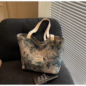 Detail of floral tapestry tote bag featuring woven straps and vintage label on a chair