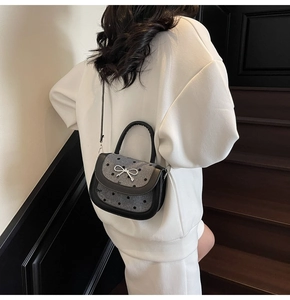 Detail of grey polka dot saddle bag with silver bow accent and black leather handle