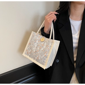 Detail of canvas tote bag with grey lace overlay and floral embroidery held by model