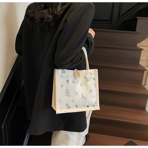 Lace-covered canvas tote with floral embroidery and wooden button held by a model
