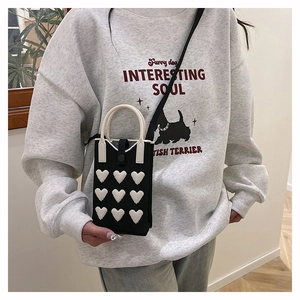 Close-up of black knit phone bag with 3D white hearts on a model with a shoulder strap