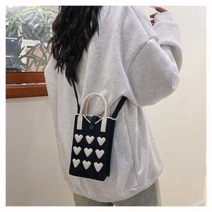 Detail of a black knitted mobile phone bag with white heart patterns worn by a model