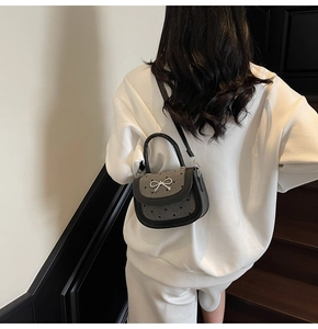 Detailed view of grey wool crossbody bag with metal bow and heart patterns on a model