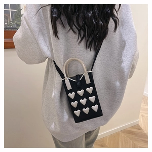 Detailed back view of a black knitted phone bag with white 3D heart motifs and strap
