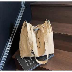 Close-up of khaki drawstring bucket bag with textured fabric on a wooden staircase