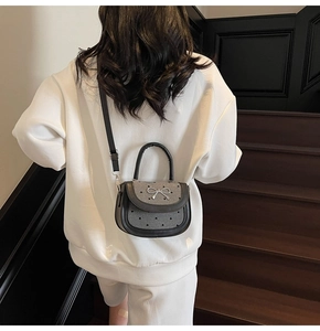 Detail of black saddle bag with bow accent and heart pattern worn over the shoulder
