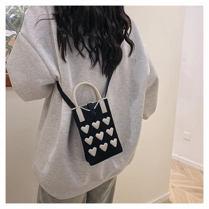 Detail of knitted black phone bag with white heart appliques and curved handle strap