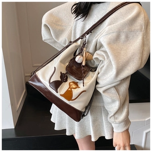 Détail du sac cabas bicolore avec appliques de chat et breloques porté par un mannequin