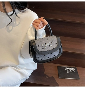 Close-up of silver bow buckle and polka dot pattern on grey faux leather handbag