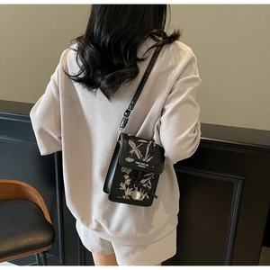 Detail of floral embroidery and brand logo on a compact black crossbody bag