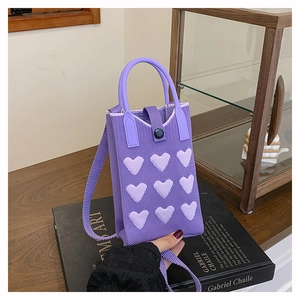 Close-up of purple knitted handbag featuring pink heart patterns and thick texture