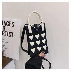 Detail of a black knitted mini bag with white 3D heart patterns and sturdy U-shaped handles