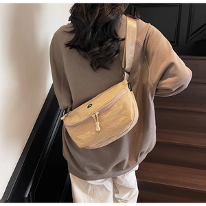 Dettaglio della borsa a mezzaluna beige con logo JL indossata su scale in legno