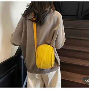 Détail d'un sac bandoulière jaune en nylon avec broderie sur fond d'escalier