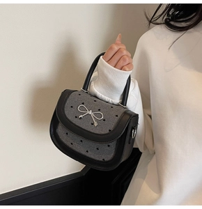 Close-up of heart laser-cut texture and silver bow detail on gray fabric baguette bag