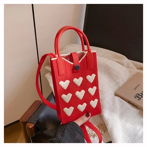 Detail of red knitted phone bag with white hearts showing strap and button closure