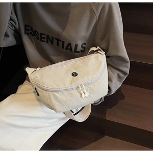 Dettaglio della borsa a mezzaluna crema con doppie cerniere e logo JL rotondo