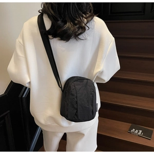 Détail d'un mini sac à bandoulière en nylon noir porté par un mannequin en style urbain