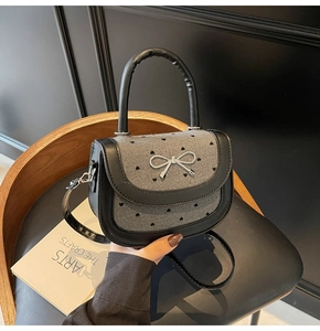Detail of grey fabric bag with black heart embroidery and silver bow metal buckle