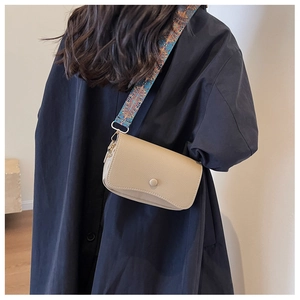 Detail view of beige pebbled leather crossbody bag with ethnic style wide strap on model