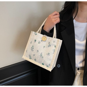 Close-up of white canvas handbag with lace floral embroidery and round wooden button closure
