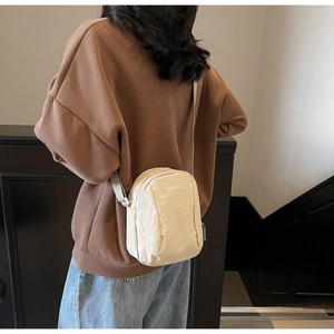 Gros plan d'un mini sac bandoulière crème montrant la toile texturée et la sangle réglable