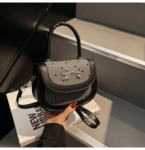 Detail showing bow metal buckle and textured fabric with heart patterns on saddle bag