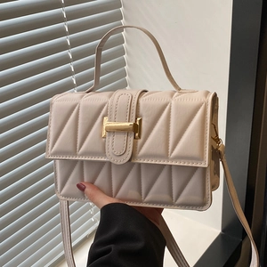 Quilted cream crossbody bag with gold buckle and top handle held against shutters
