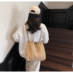 Detail of khaki drawstring bucket bag with external pockets worn by model