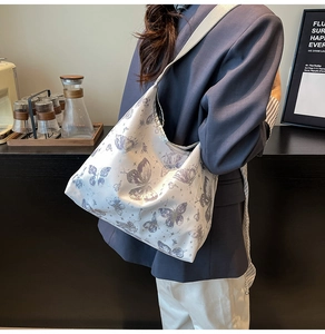 Scatto lifestyle di una grande borsa a spalla bianca con stampa di farfalle viola chic