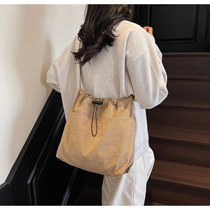 Detail of light khaki drawstring bucket bag with front pockets on a casual model