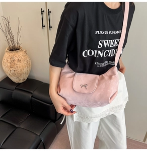 Sac demi-lune en daim rose avec nœud argenté porté par un mannequin en décor épuré