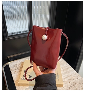 Macro shot of dark burgundy patent leather mini bag featuring a large pearl buckle detail