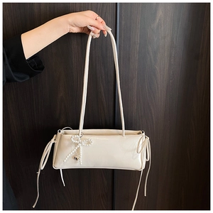Detail of cream underarm bag featuring glossy PU texture and pearl bow charm accessory