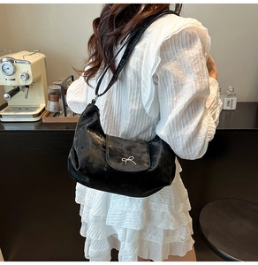 Détail d'un sac demi-lune noir brillant avec un nœud argenté sur une table de café