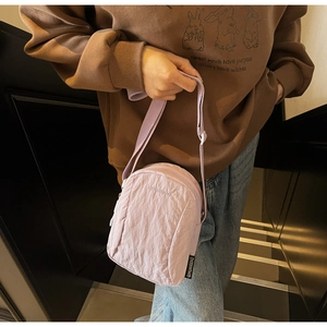 Mini sac bandoulière en nylon violet clair avec logo porté par un mannequin en ville