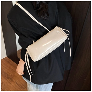 Detail of cream glossy shoulder bag with ribbon drawstrings and sleek cylindrical design