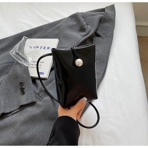 Detail of glossy black mini crossbody bag featuring a large pearl clasp and thin strap